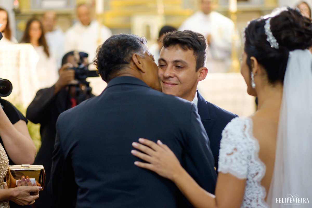 pai da noiva dando um beijo no rosto do genro quando a entrega a ele no altar em casamento na igrejinha velha em guarapari em foto feita por felipe vieira fotografo de casamentos em guarapari