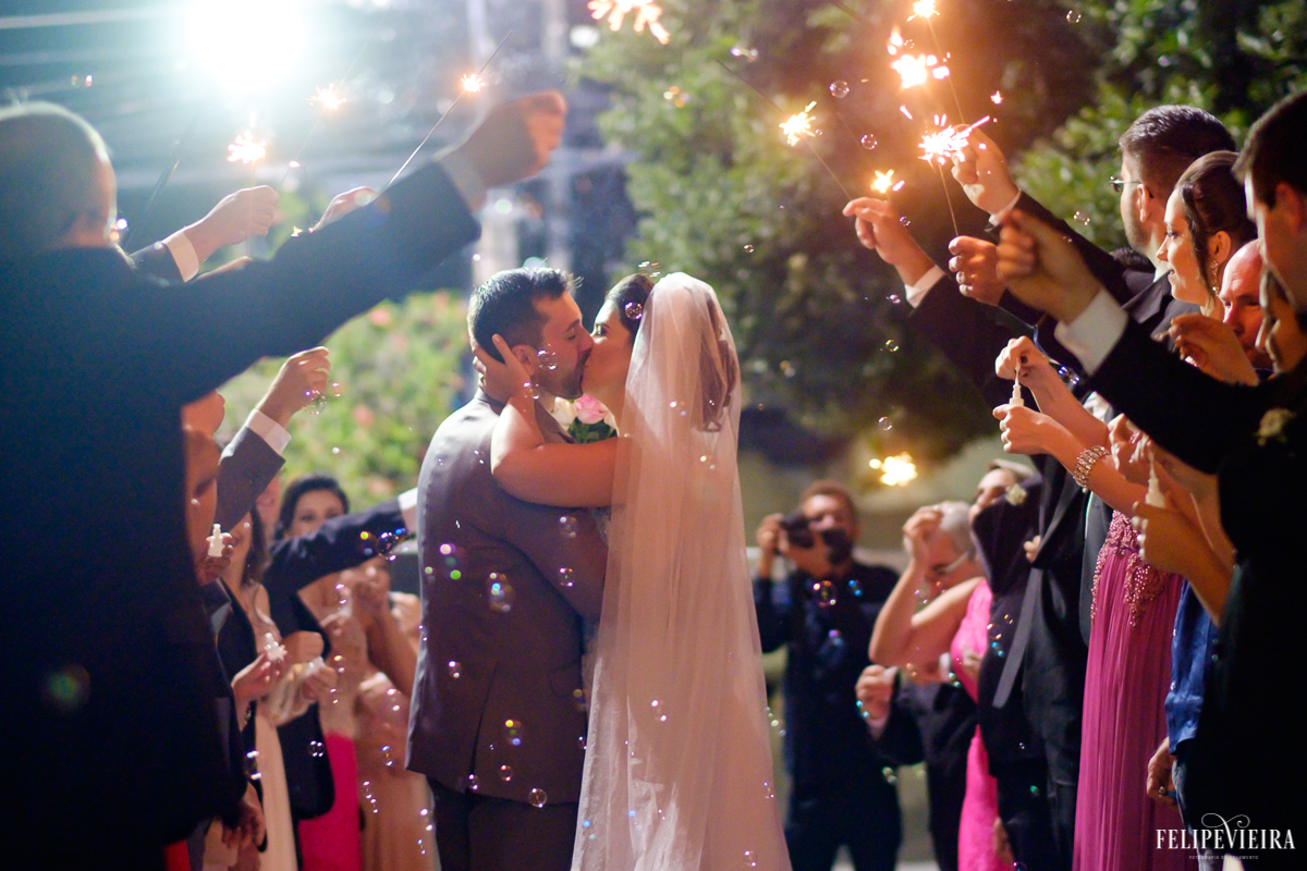 noivos se beijando já fora da igreja com seus padrinhos ao redor e jogando bolhas neles foto feita por felipe vieira fotografo de casamentos em guarapari