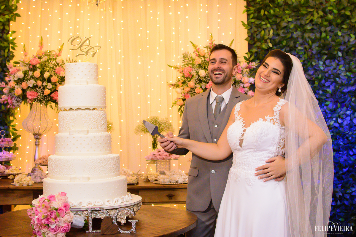 Noivos sorrindo ao cortarem o bolo foto feita por felipe vieira fotografo de casamentos em guarapari