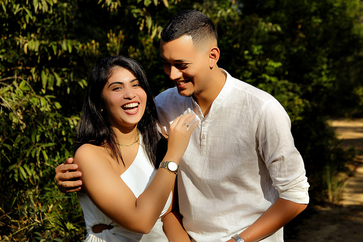 Casal sorrindo em ensaio pré-casamento em Guarapari ele veste bata branca ela vestido branco foto ao ar livre por fotógrafo especializado em casamentos destacando a alegria e o romance do casal