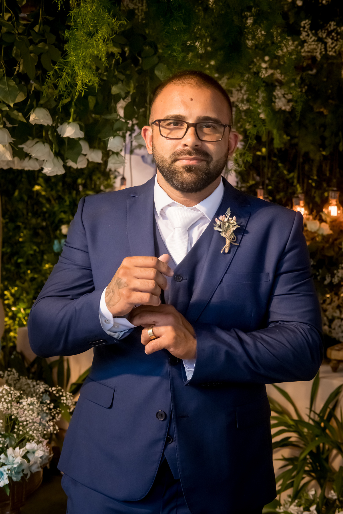 retrato do novo na festa em frente a mesa do bolo com o noivo segunrado e acertando o punho da camisa sob um treno azul 