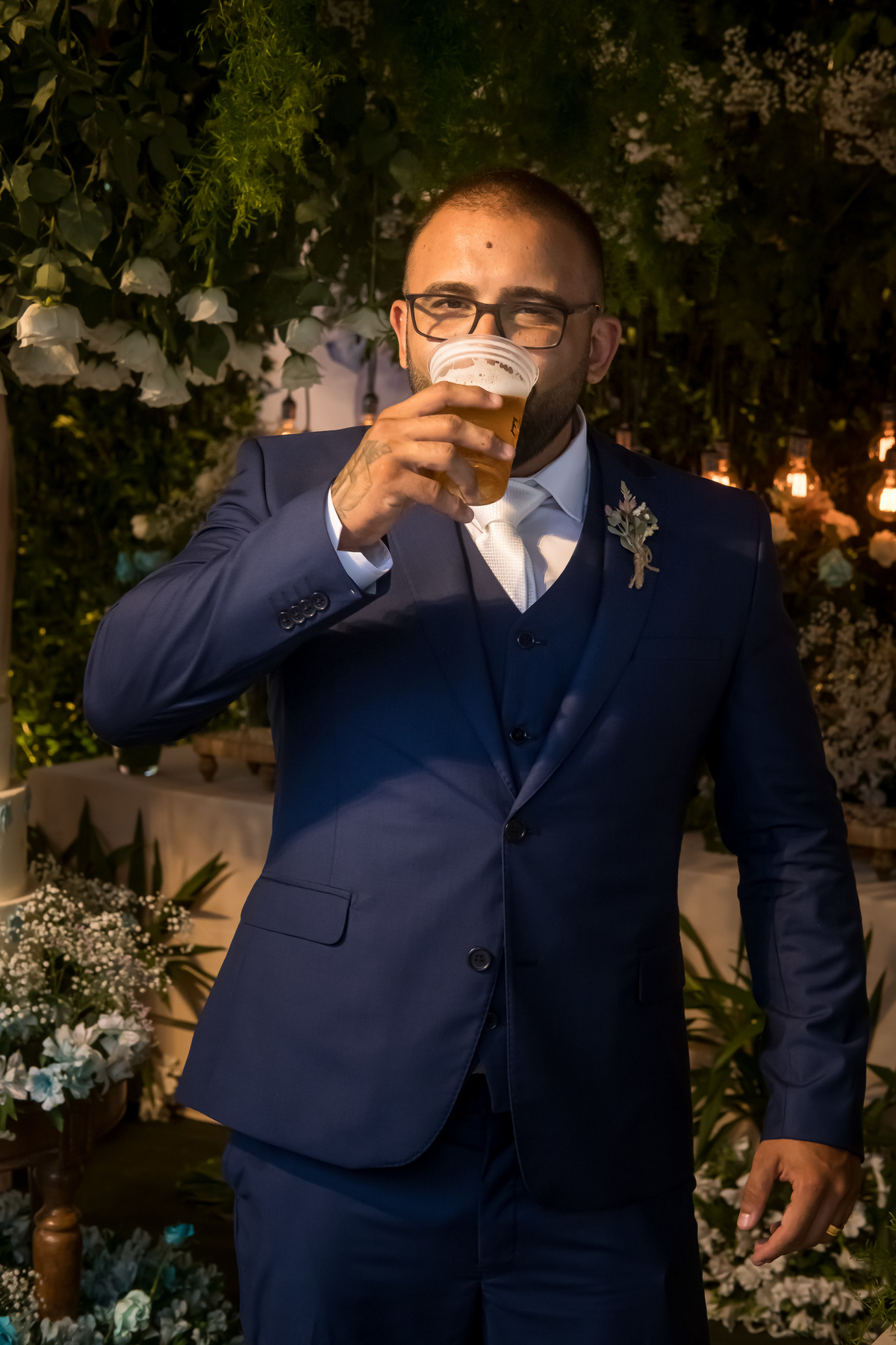 retrato do noivo bebendo uma dose de whisky em frente a mesa do bolo 