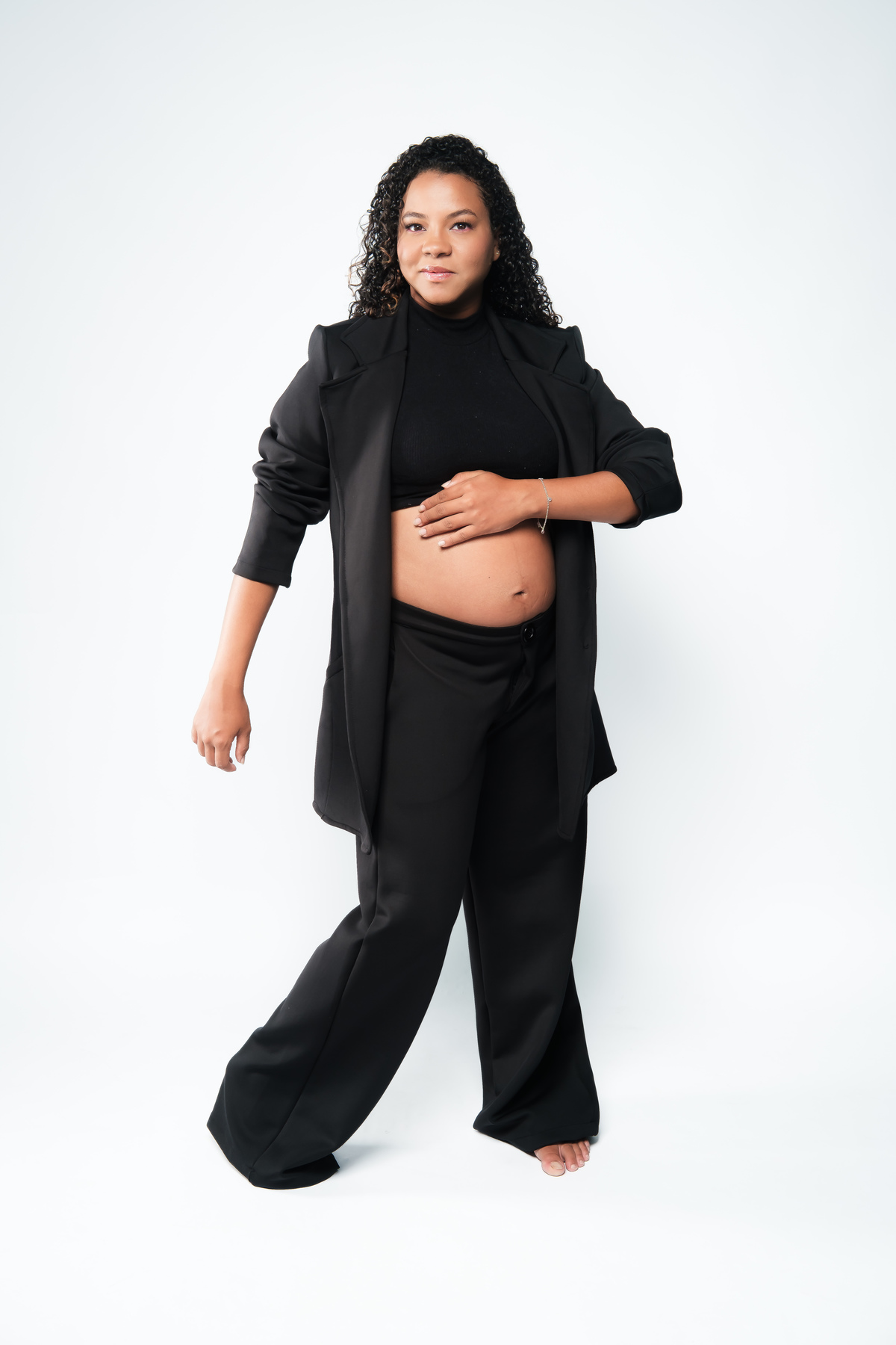 Book de gestante com fundo neutro e luz suave no estúdio. Sessão de fotos de grávida com roupa clássica e feminina.