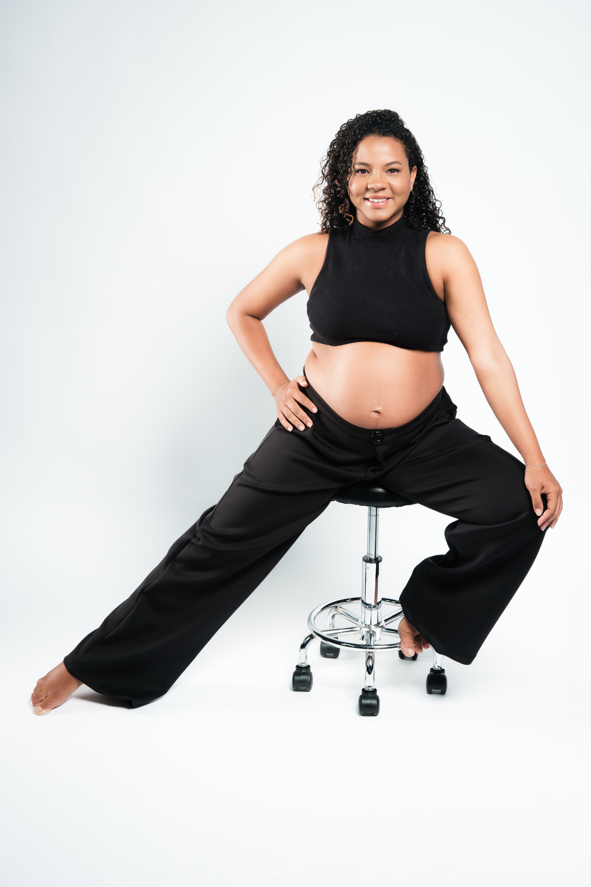 Ensaio de gestante em estúdio com iluminação natural. Fotografia de grávida com destaque na barriga e expressão.