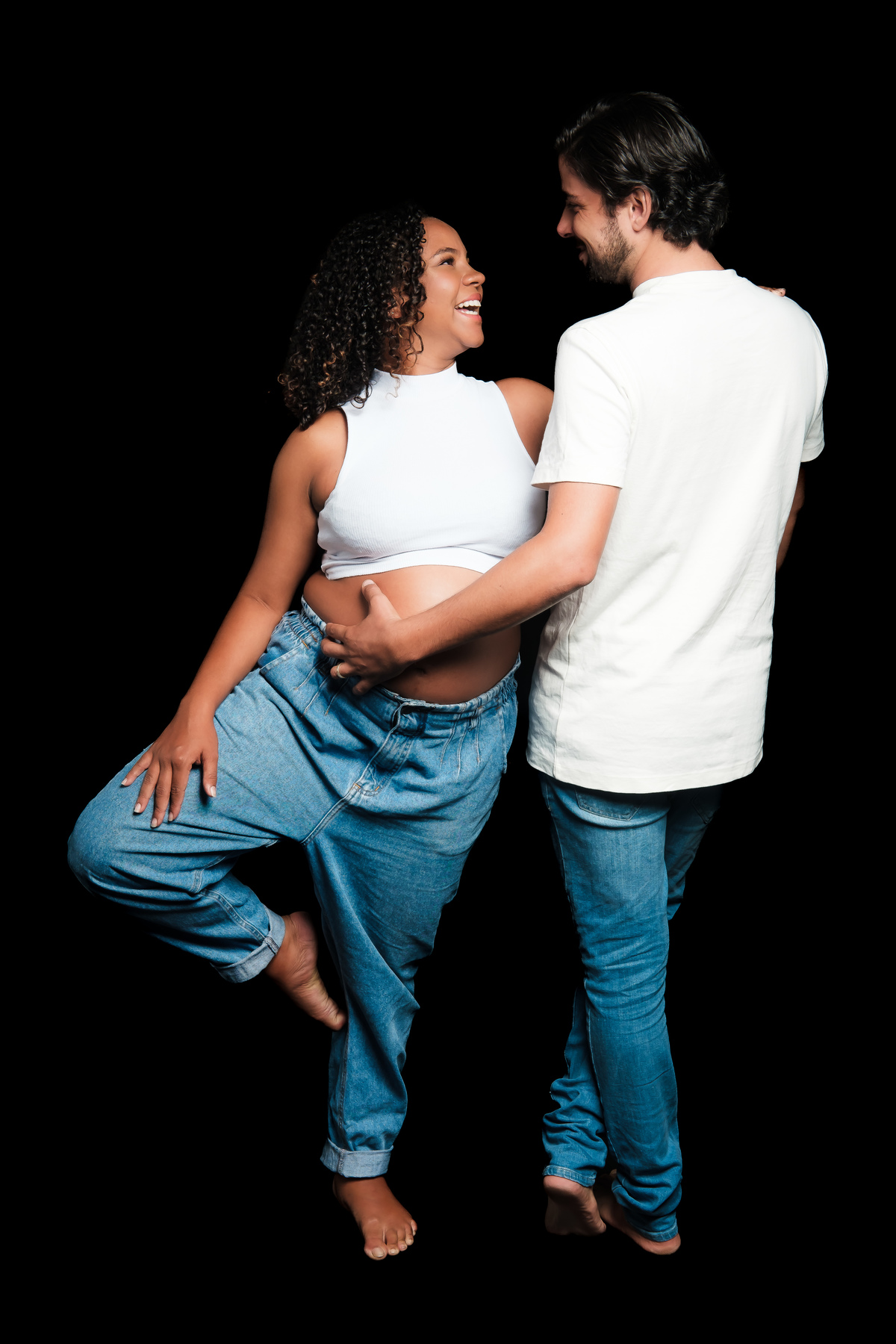 Sessão de fotos de grávida em estúdio com fundo branco e luz suave. Ensaio de gestante com roupas discretas e postura relaxada.