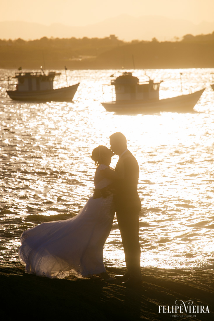 silhueta de noivos com barquinhos ao fundo e luz do sol no mar foto feita por felipe vieira fotografo de casamentos em guarapari