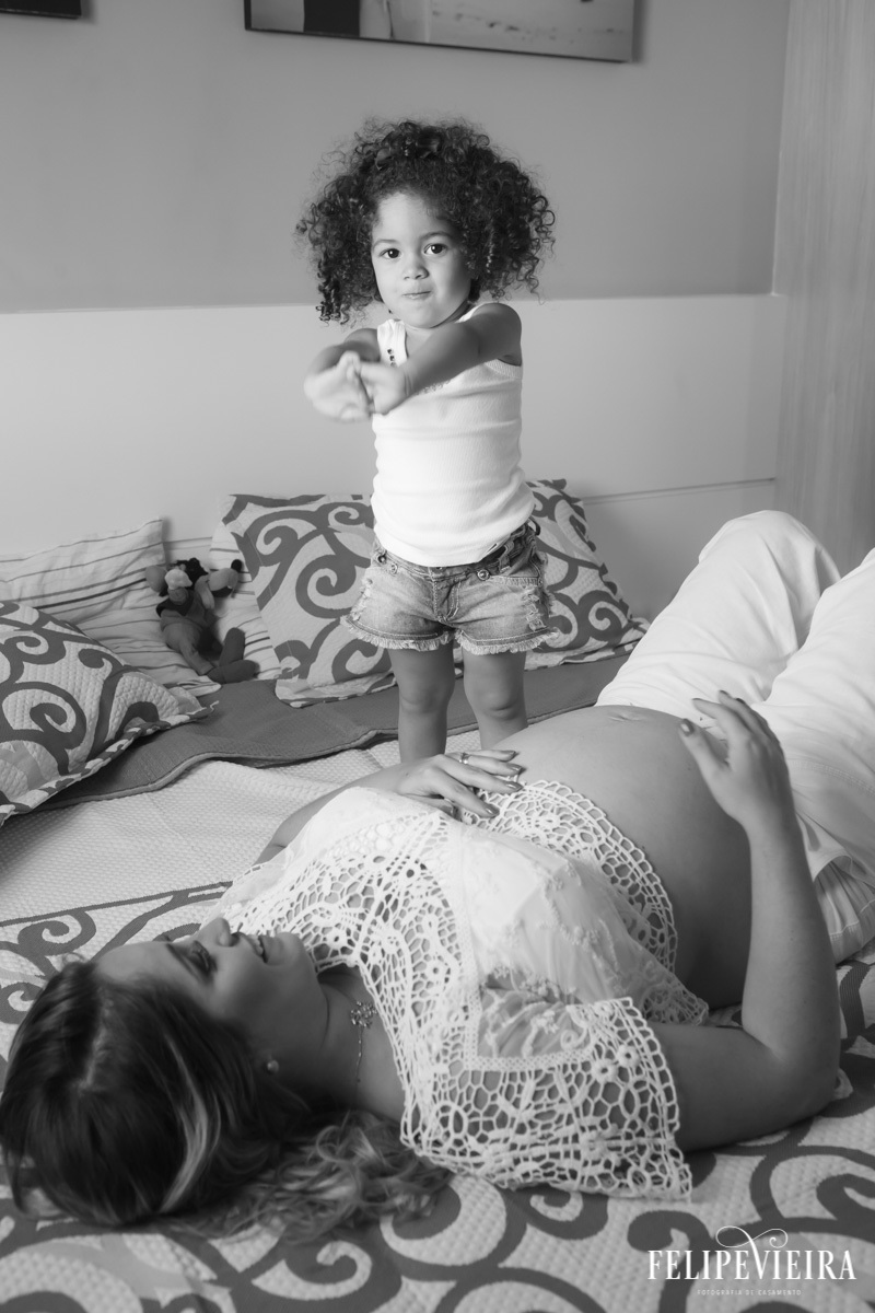 mãe deitada e sorrindo com a filha a olhar para sua barriga em foto feita por felipe vieira fotógrafo em guarapari espírito santo