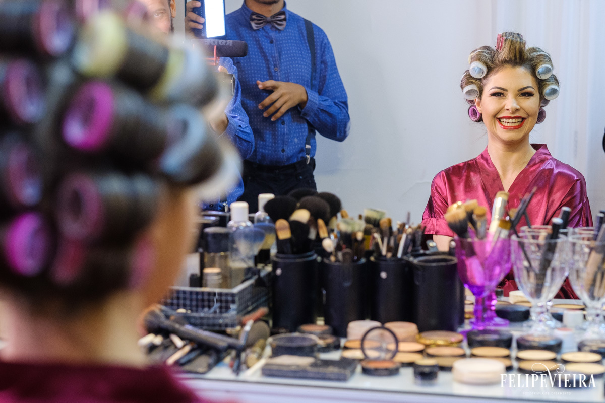 Noiva no espelho sorrindo ao fazer a maquiagem foto felipe vieira fotografo de casamentos guarapari