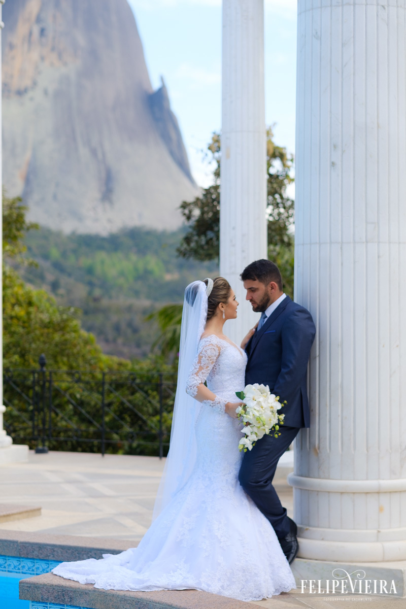 noivos se olhando apoiados em pilastra com a pedra azul de fundo foto felipe vieira fotografo de casamentos guarapari