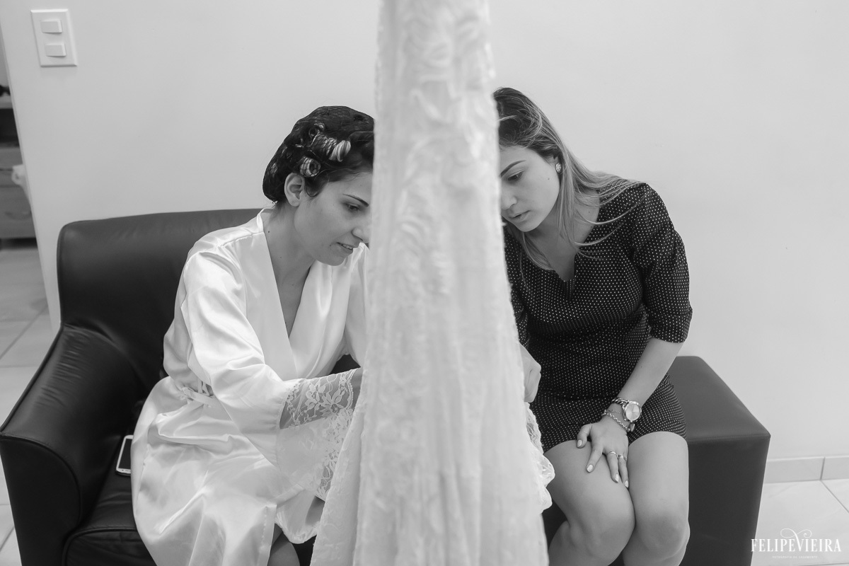 noiva e madrinha mexendo no vestido e sorrindo  enquanto se arrumam para o casamento em feita por Felipe Vieira fotografo de casamentos em guarapari e grande vitória