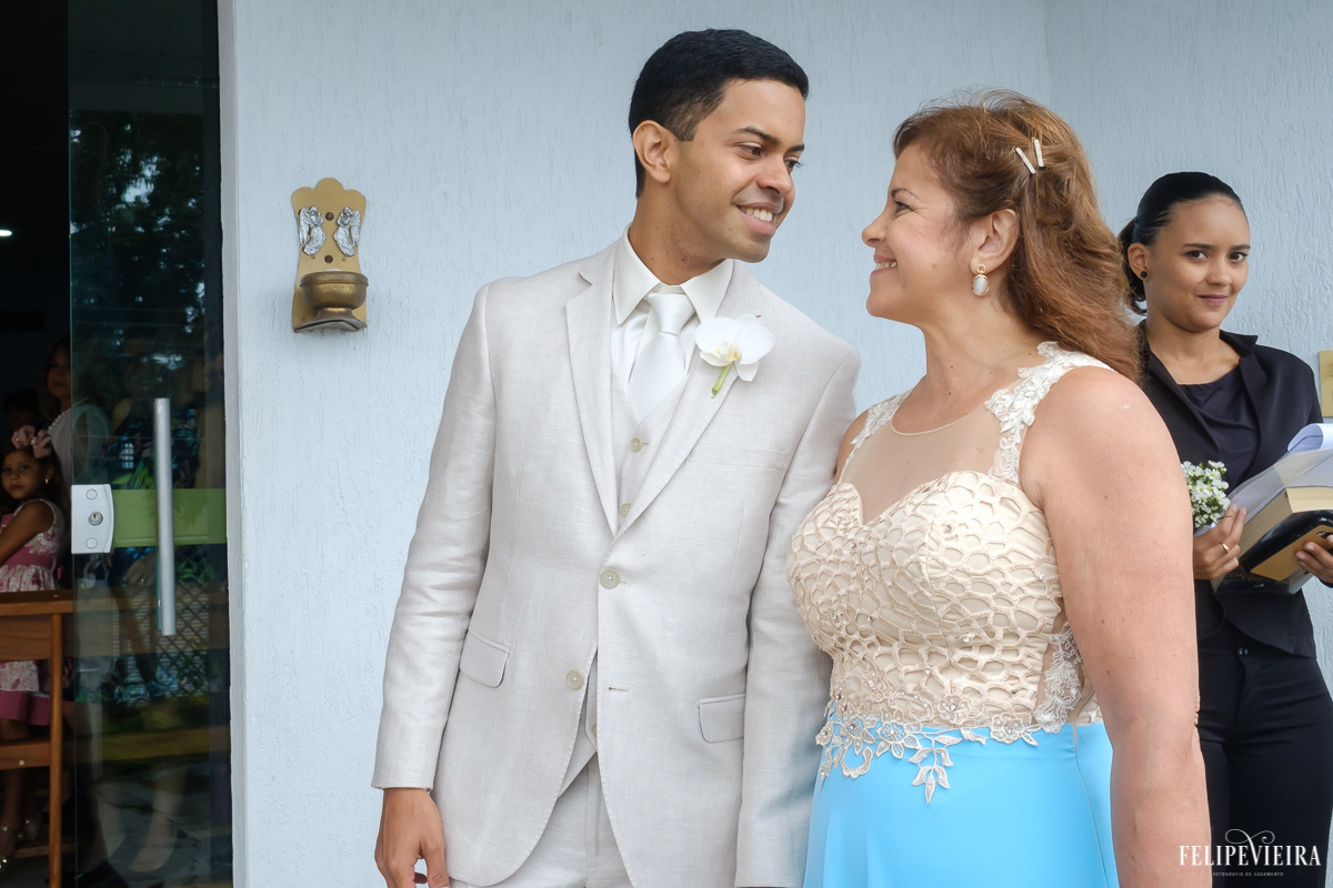 noivo entrando na igreja com a sua mãe e sorrindo para ela em feita por Felipe Vieira fotografo de casamentos em guarapari e grande vitória