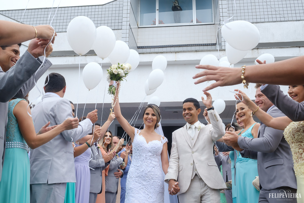 noivos saindo da igreja com os padrinhos segurando balões para festejar em feita por Felipe Vieira fotografo de casamentos em guarapari e grande vitória