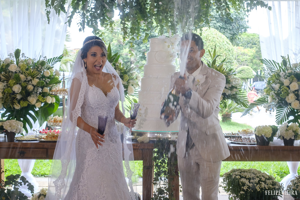 noivos estourando o champanhe na mesa do bolo em feita por Felipe Vieira fotografo de casamentos em guarapari e grande vitória 