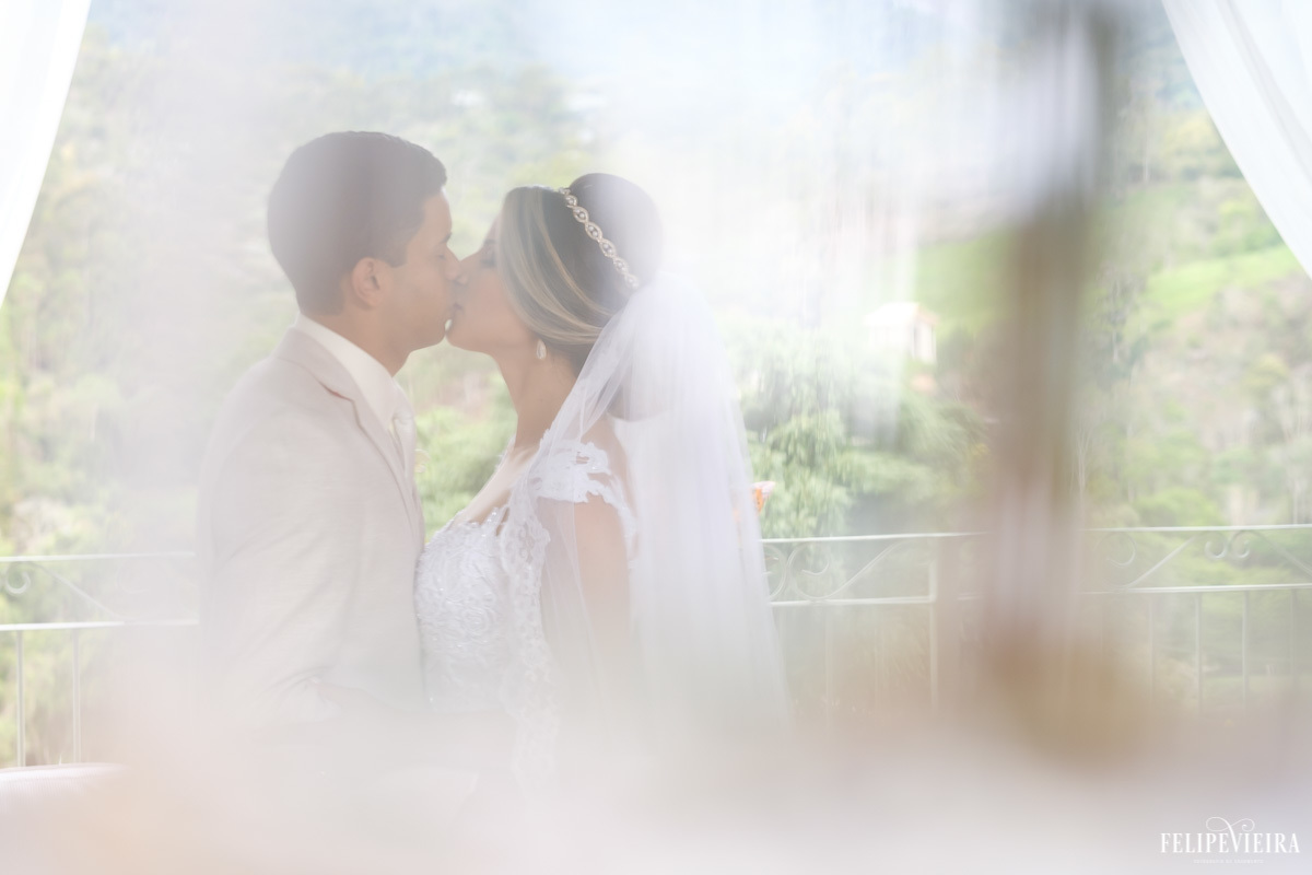 foto de noivos se beijando com véu da noiva na frente da foto causando um efeito diferente em ensaio externo em feita por Felipe Vieira fotografo de casamentos em guarapari e grande vitória