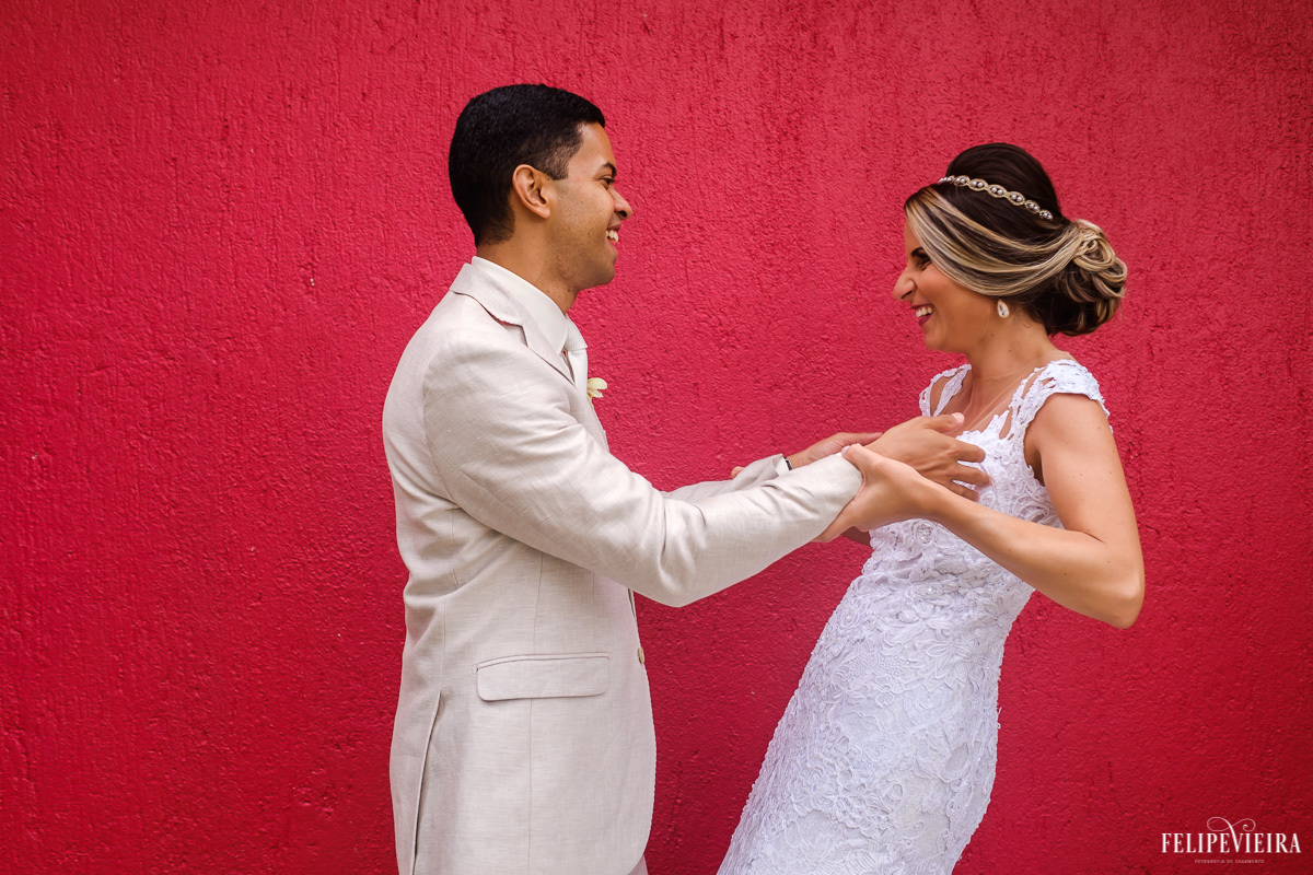 noivos brincando e rindo em frente a uma parede vermelha em ensaio externo em feita por Felipe Vieira fotografo de casamentos em guarapari e grande vitória