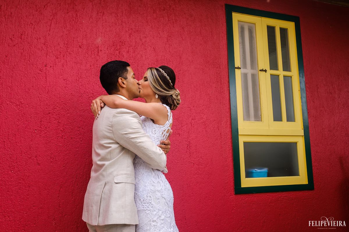 brincadeira de cores com parede vermelha e janela verde e amarela e com noivos se beijando em ensaio externo em feita por Felipe Vieira fotografo de casamentos em guarapari e grande vitória