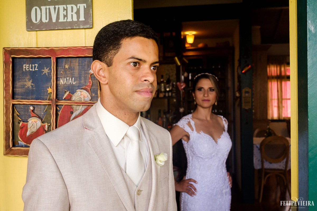 noivo em primeiro plano e noiva ao fundo olhando para ele em ensaio externo em feita por Felipe Vieira fotografo de casamentos em guarapari e grande vitória