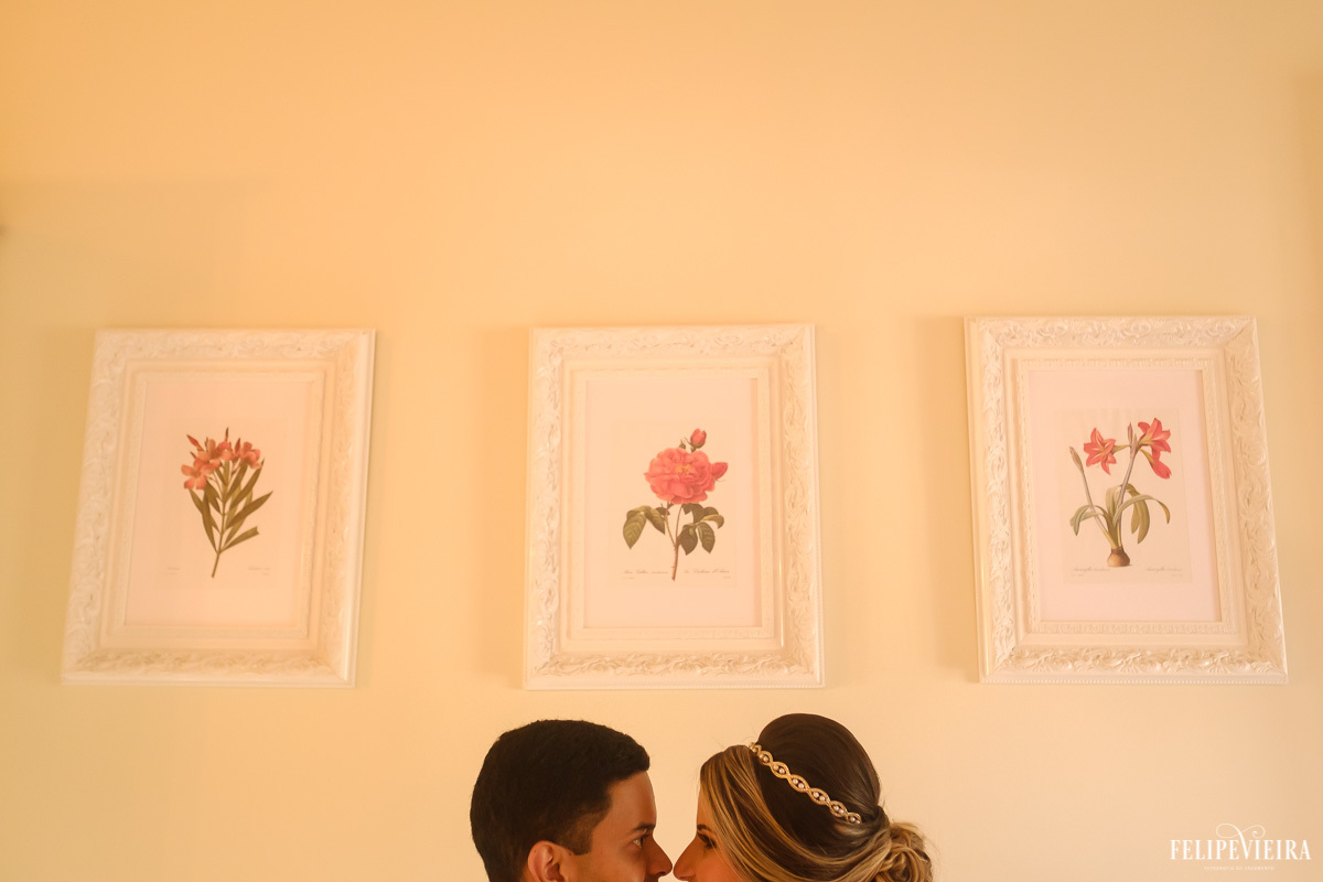 noivos de frente um para o outro e sorrindo com composição de quadros ao fundo em ensaio externo em feita por Felipe Vieira fotografo de casamentos em guarapari e grande vitória