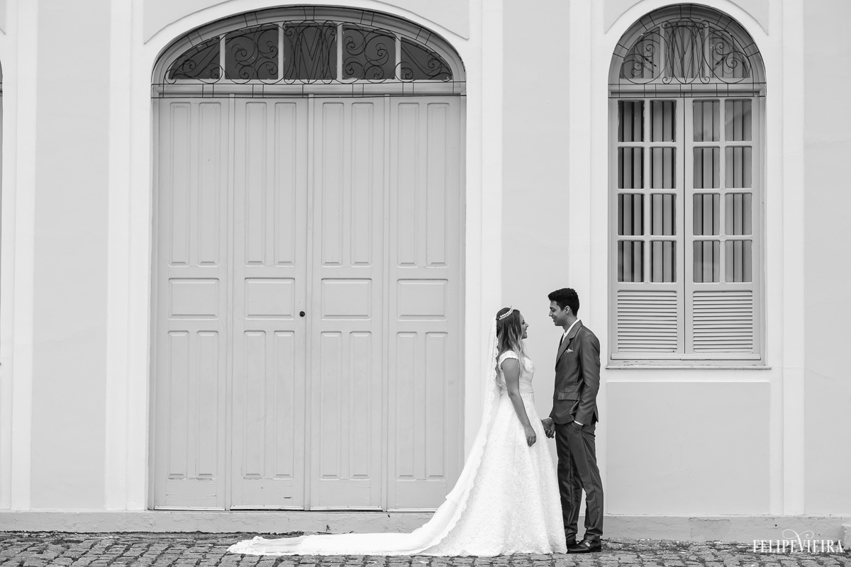 Noivos de frente um para o outro com o véu da noiva aberto com composição de porta e janela em foto em preto e branco feita por Felipe Vieira fotografo de casamentos em guarapari e grande vitória