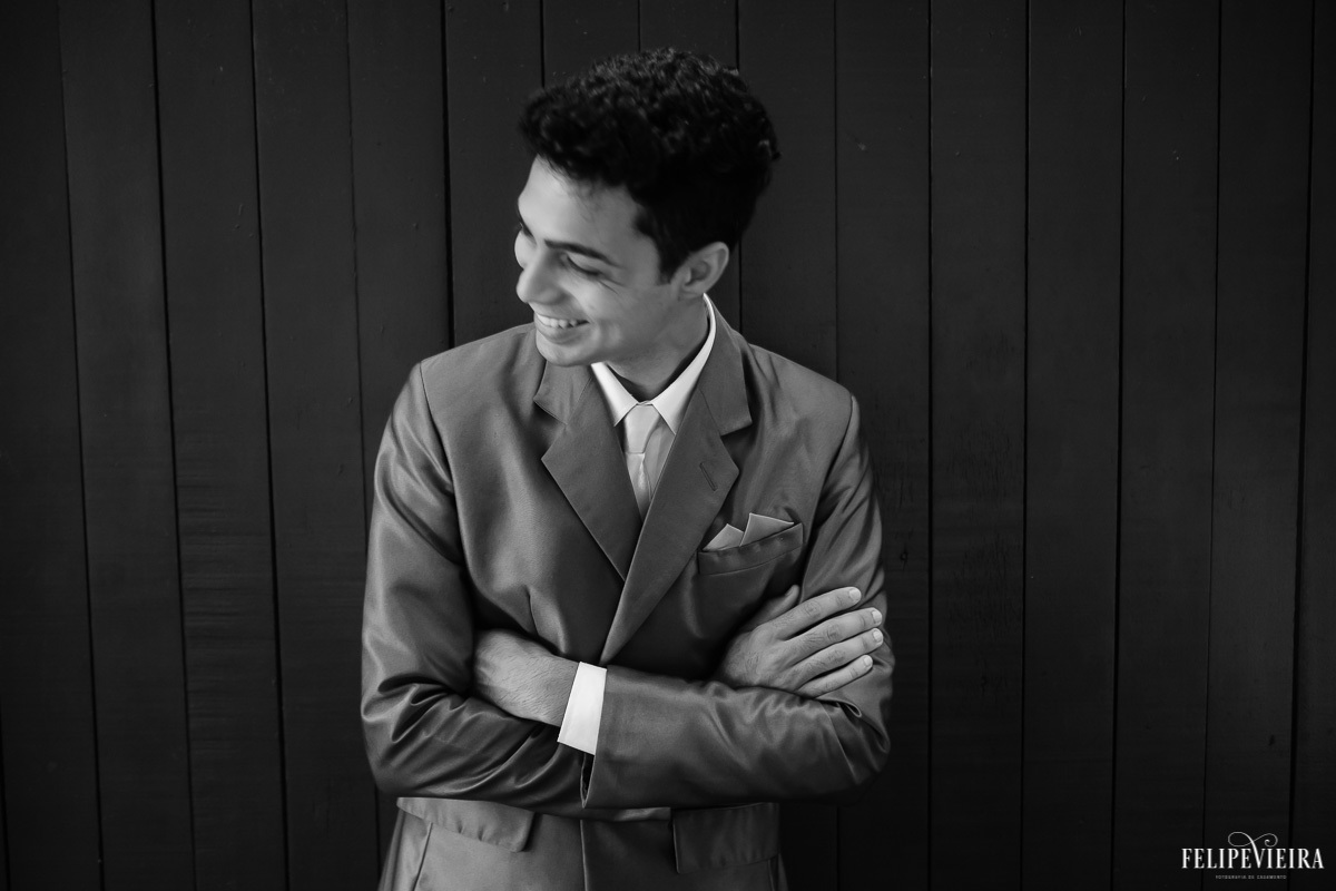 noivo de braços cruzados e sorrindo com detalhes do paletó em foto em preto e branco feita por Felipe Vieira fotografo de casamentos em guarapari e grande vitória