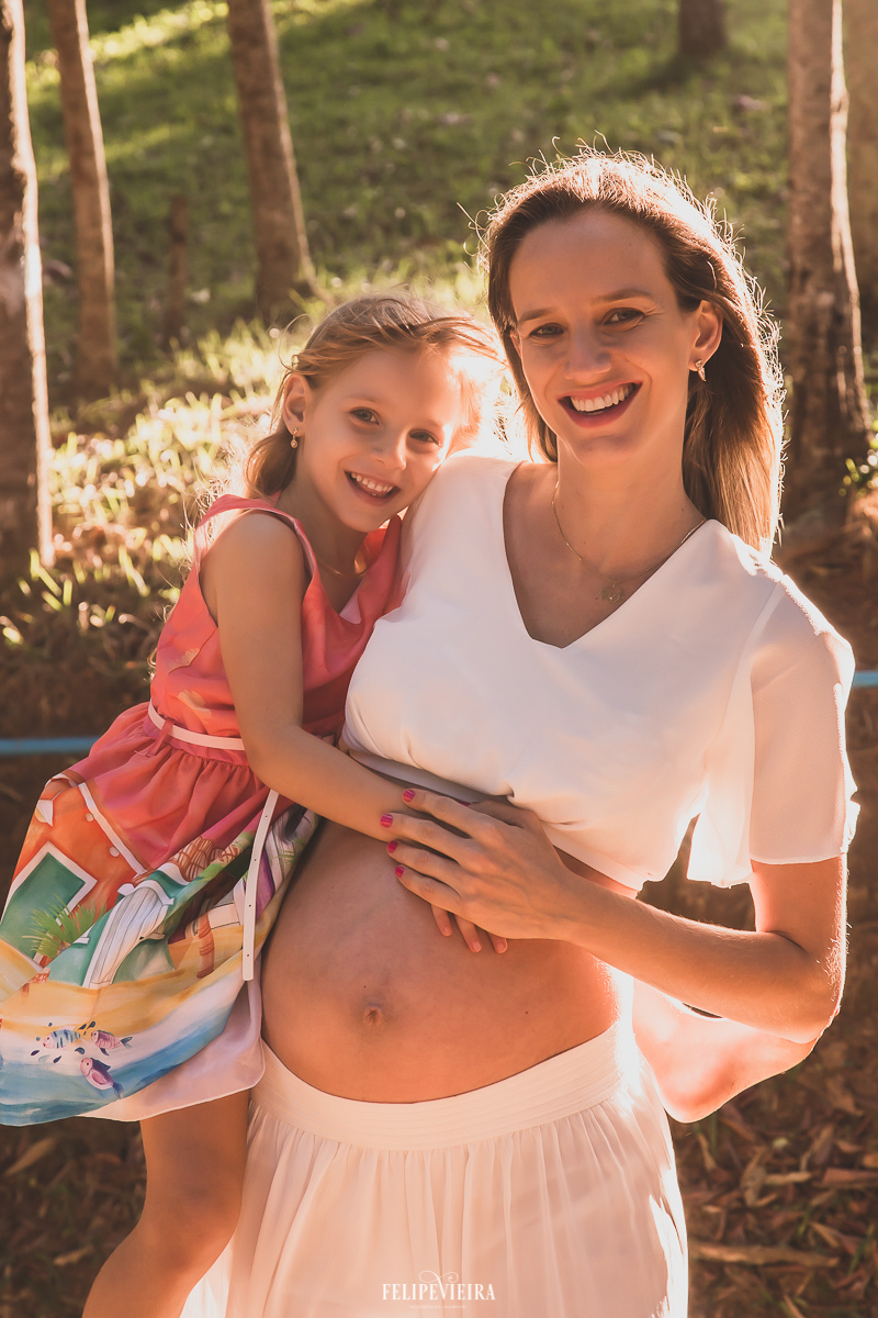 gestante com a filha no colo com 33 semanas de gestação sorrindo durante ensaio de grávida com 8 meses  com roupa para grávida