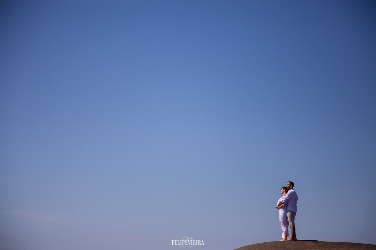 noivos em cima de uma pedra na praia em Guarapari céu azul noiva look branco