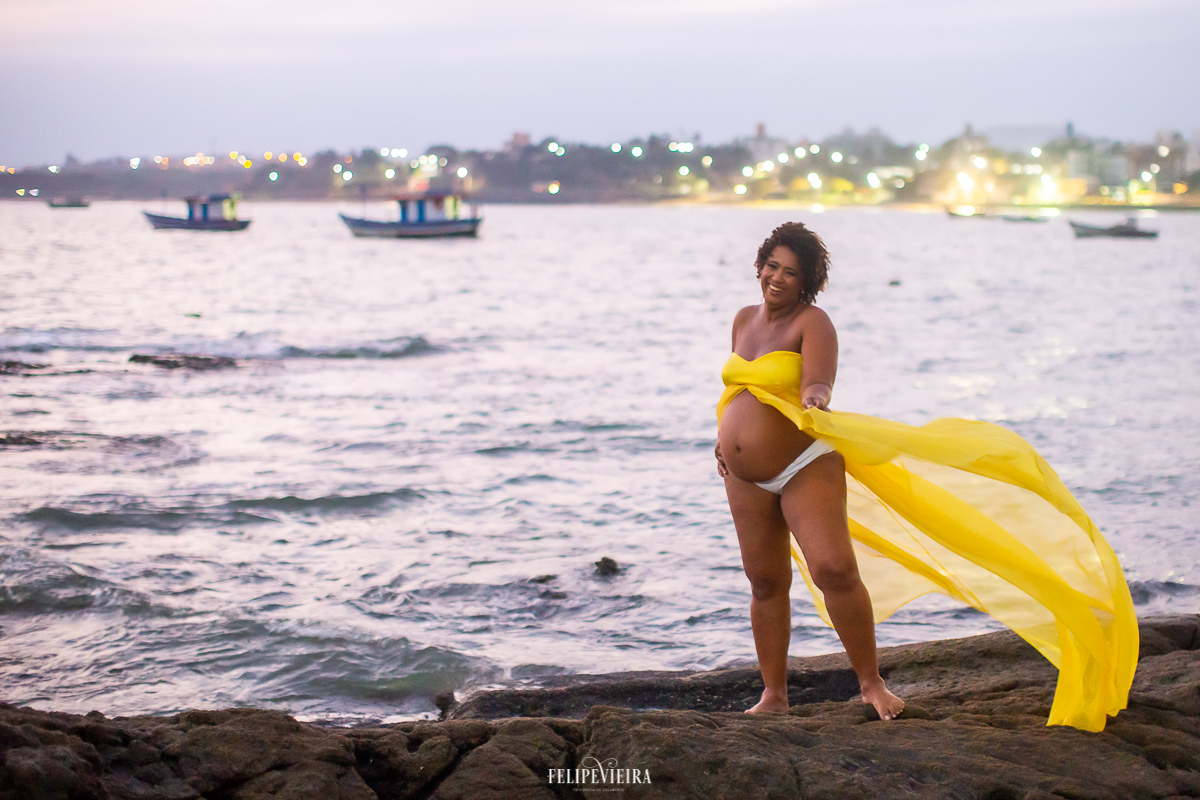 gestante de amarelo em ensaio fotográfico em cima duma pedra na praia do Urubu em Meaípe Guarapari-ES