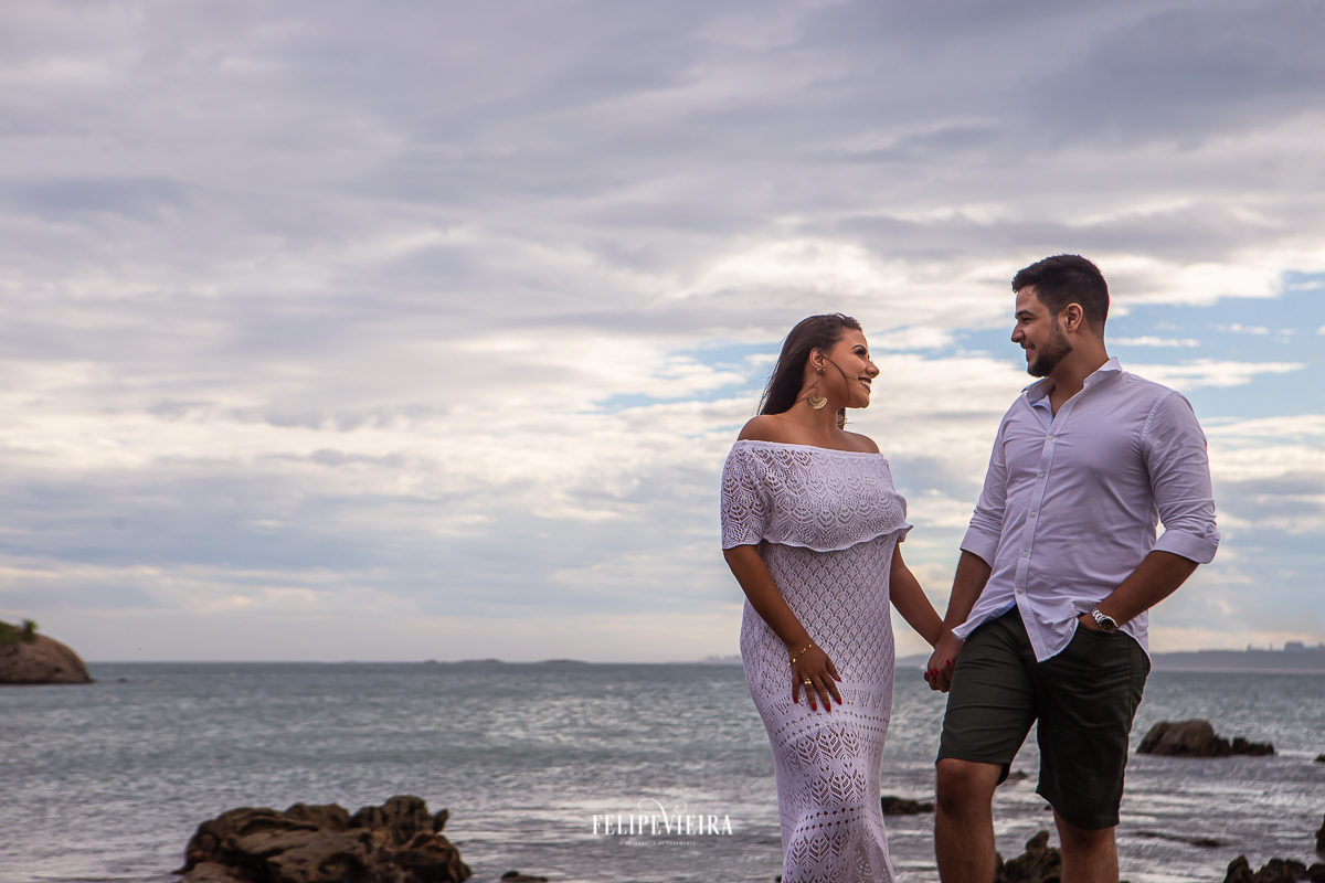 noiva com vestido de crochê branco em ensaio pré casamento com noivo de bermuda e camisa social branca nas pedras da praia de Meaípe