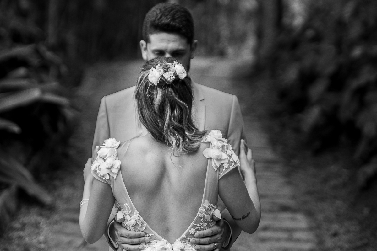 foto do decote das costas vestido da noiva com o noivo abraçando de frente