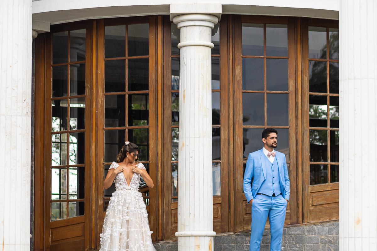 noiva ajeitando o vestido com o noivo em treno azul com as mãos no bolso
