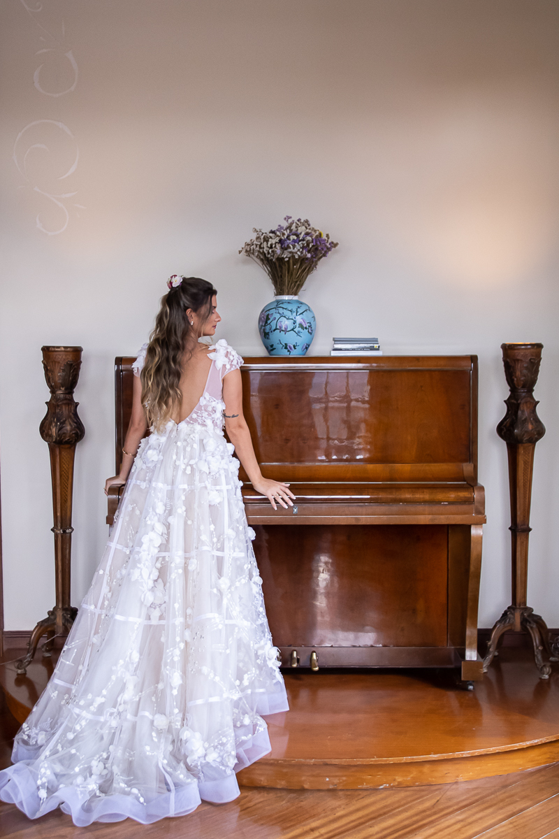 noiva de costas com vestido decotado apoiada no piano