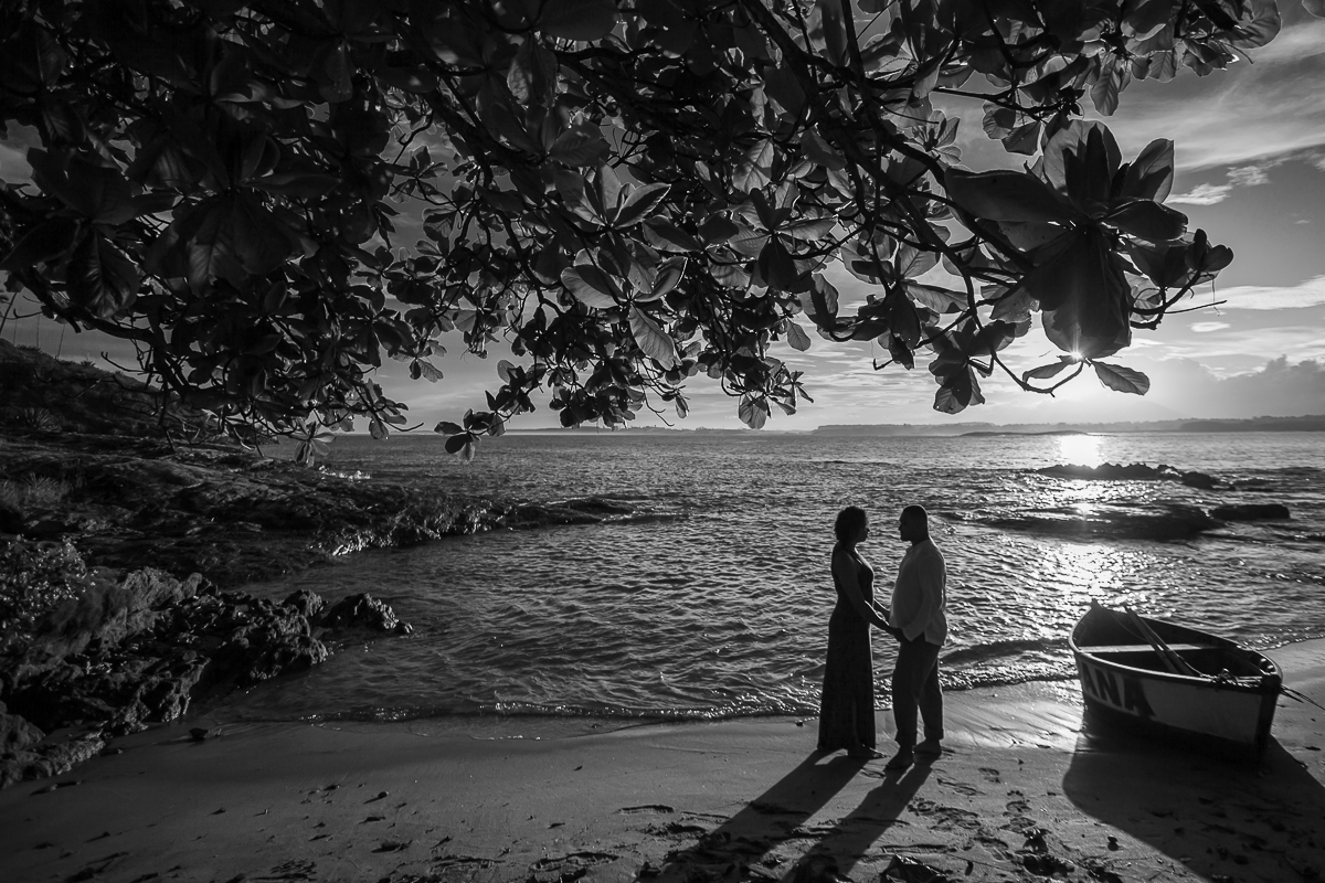 novos posando na praia durante por do sol com um barco do lado em foto em preto e branco 