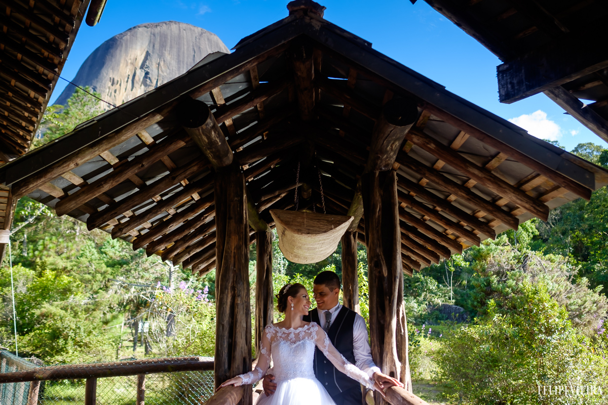 casal no lago da pousada pera azul na região serrana do espirito santo abrçados ceu azul na frente da pedra do lagarto debaixo de uma casinha de madeira com telhado