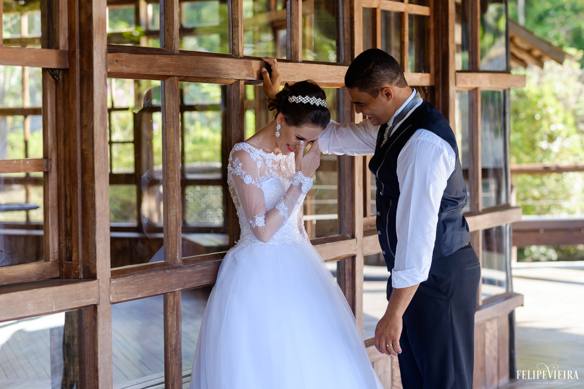 noiva rindo e noivo sorrindo encostados numa parede de vidros e madeira verde na pousada pedra azul na região serrana do estado pelo fotografo felipe vieira fvfotografo de guarapari