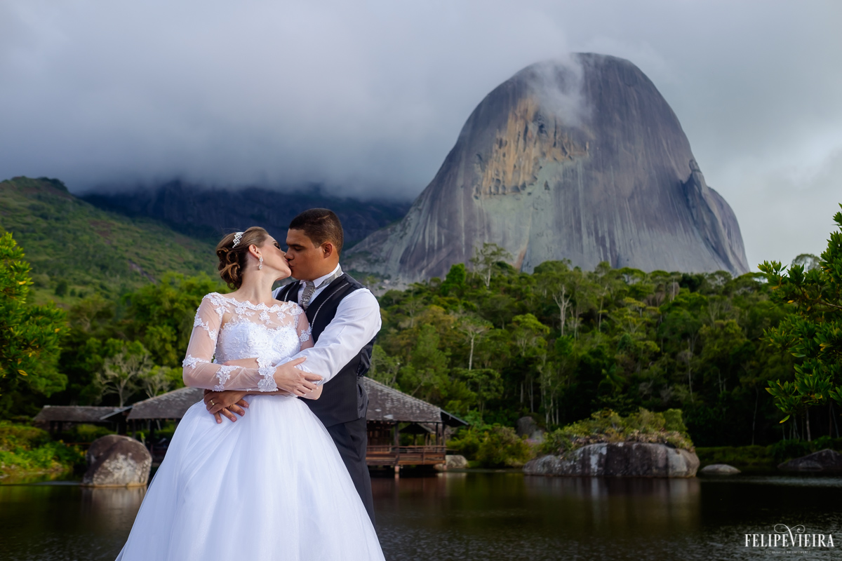 noivos se beijando na frente da pedra azul com lago ao fundo na pousada pedra azul na região serrana do estado do espirito santo fotos feitas pelo fotografo de casamento felipe vieira de guarapari