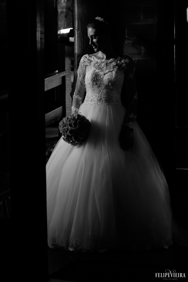 fotografia preto e branca de noiva com buqê em pé encostada na parede na pousada pedra azul fotografo de guarapari felipe vieira fvfotografo