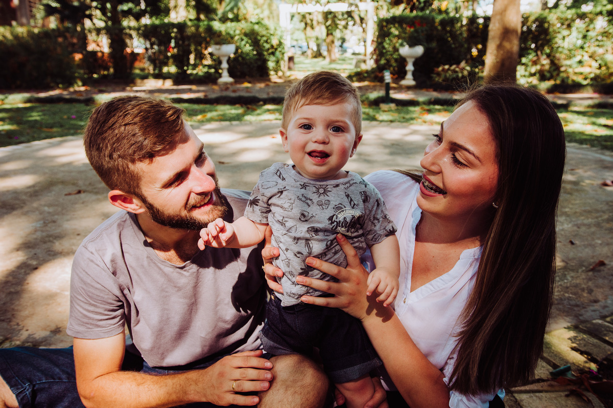 Familia sentada no chão, brincando com o filho em ensaio fotografico de 1 aninho