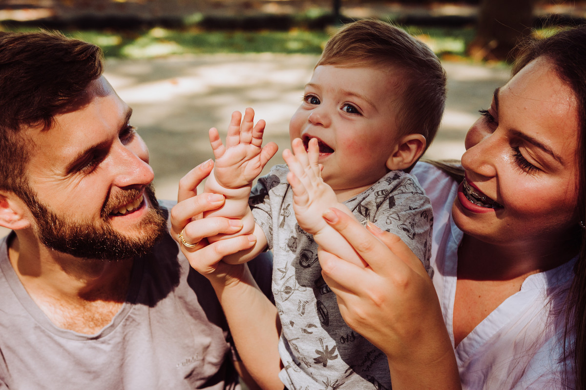 Familia sentada no chão, brincando com o filho em ensaio fotografico de 1 aninho