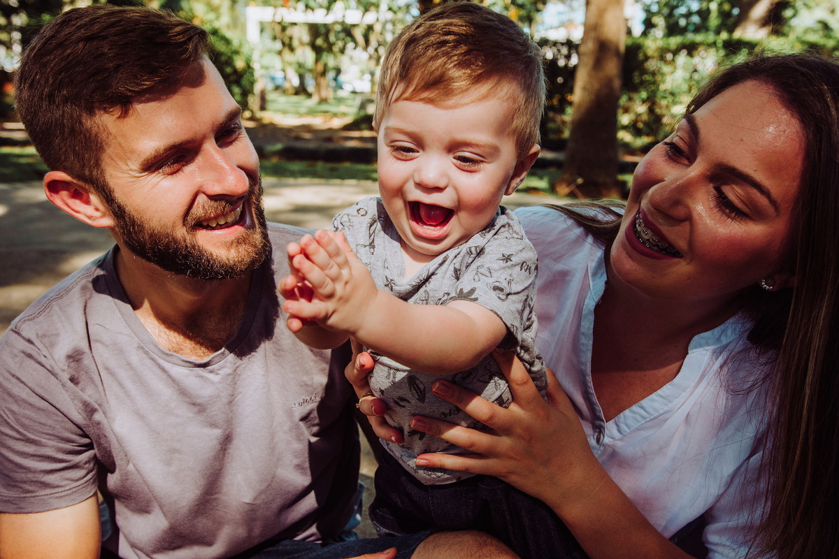 Familia sentada no chão, brincando com o filho em ensaio fotografico de 1 aninho