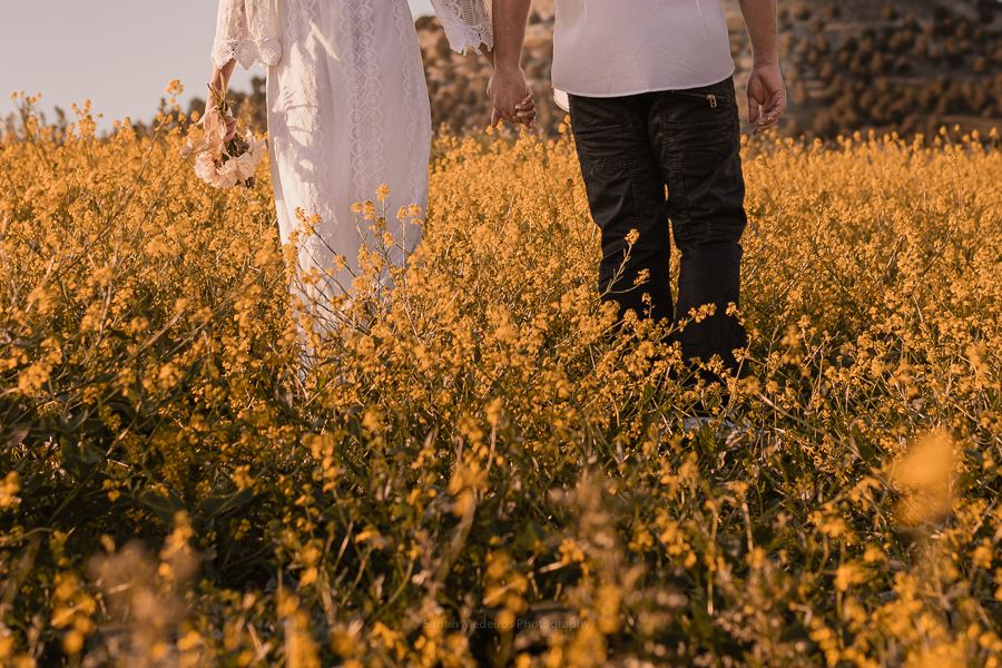 novios andando por el campo de flores amarillas