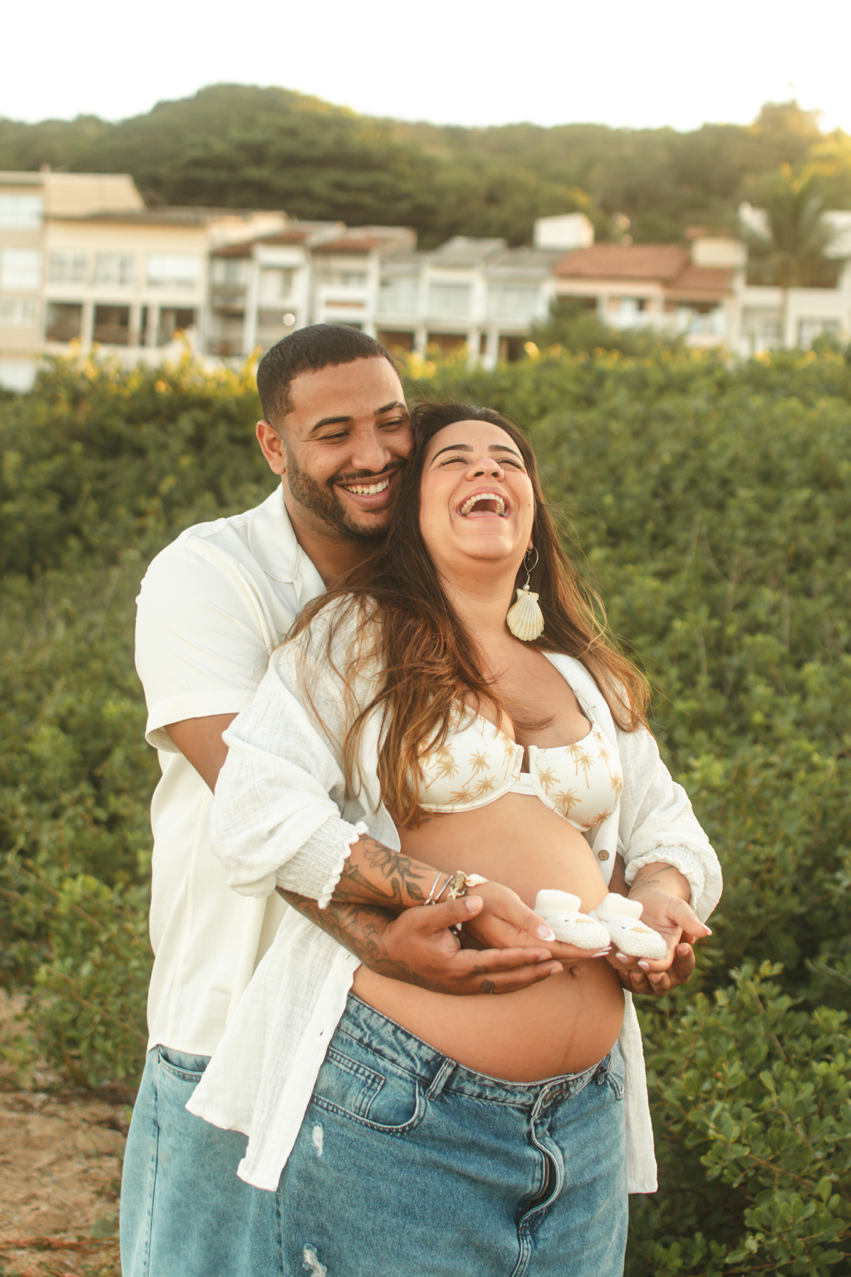 Casal sorrindo abraçados com vegetação de fundo.