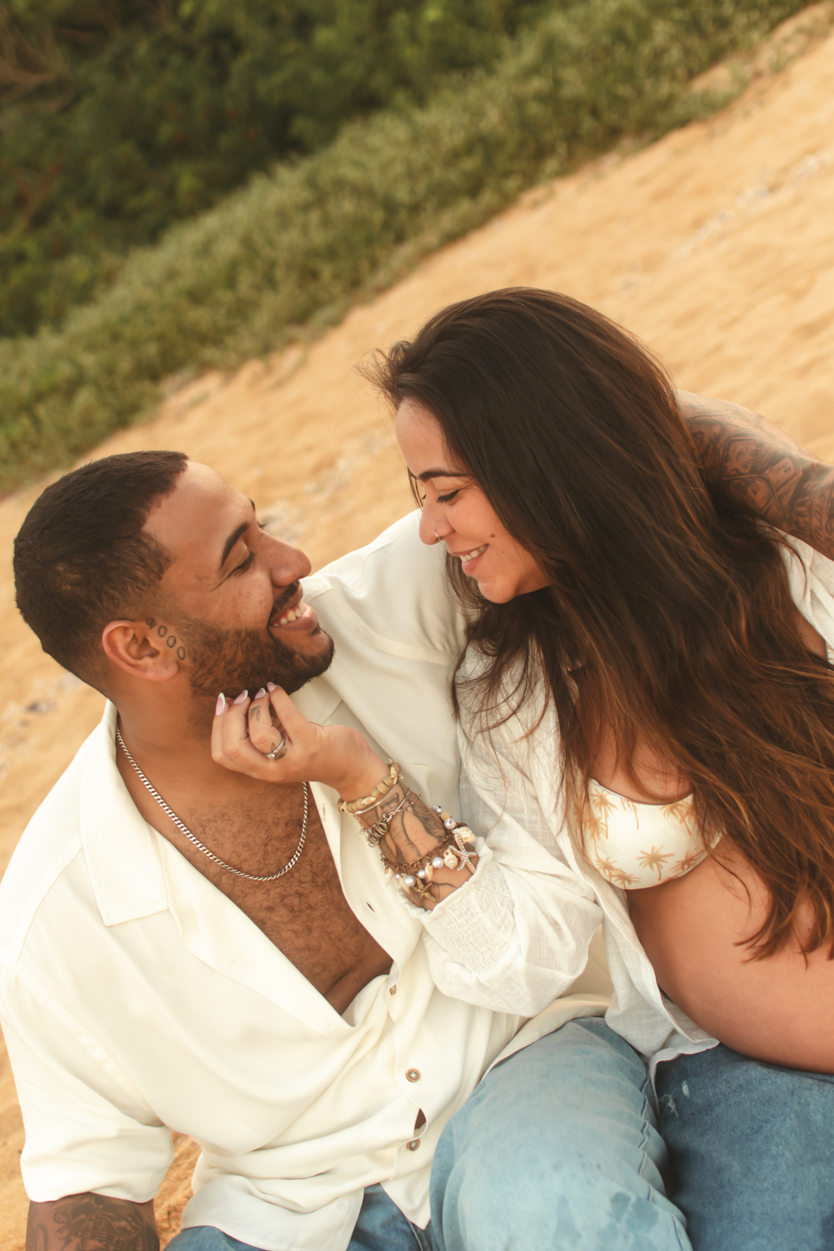 Casal trocando carinho durante ensaio fotográfico de gestante na praia.
