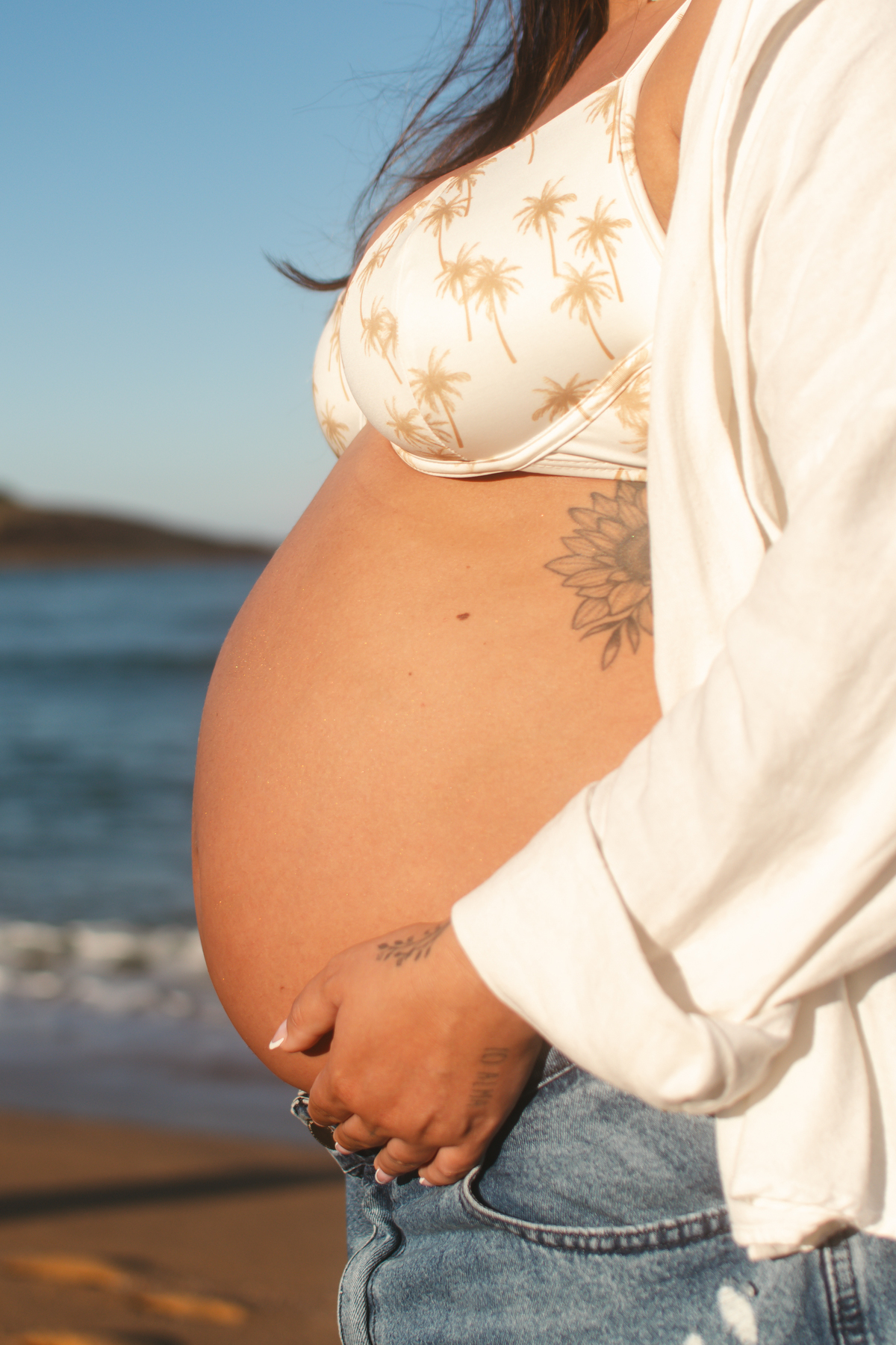 Detalhe da barriga da gestante registrado durante ensaio fotográfico na praia.