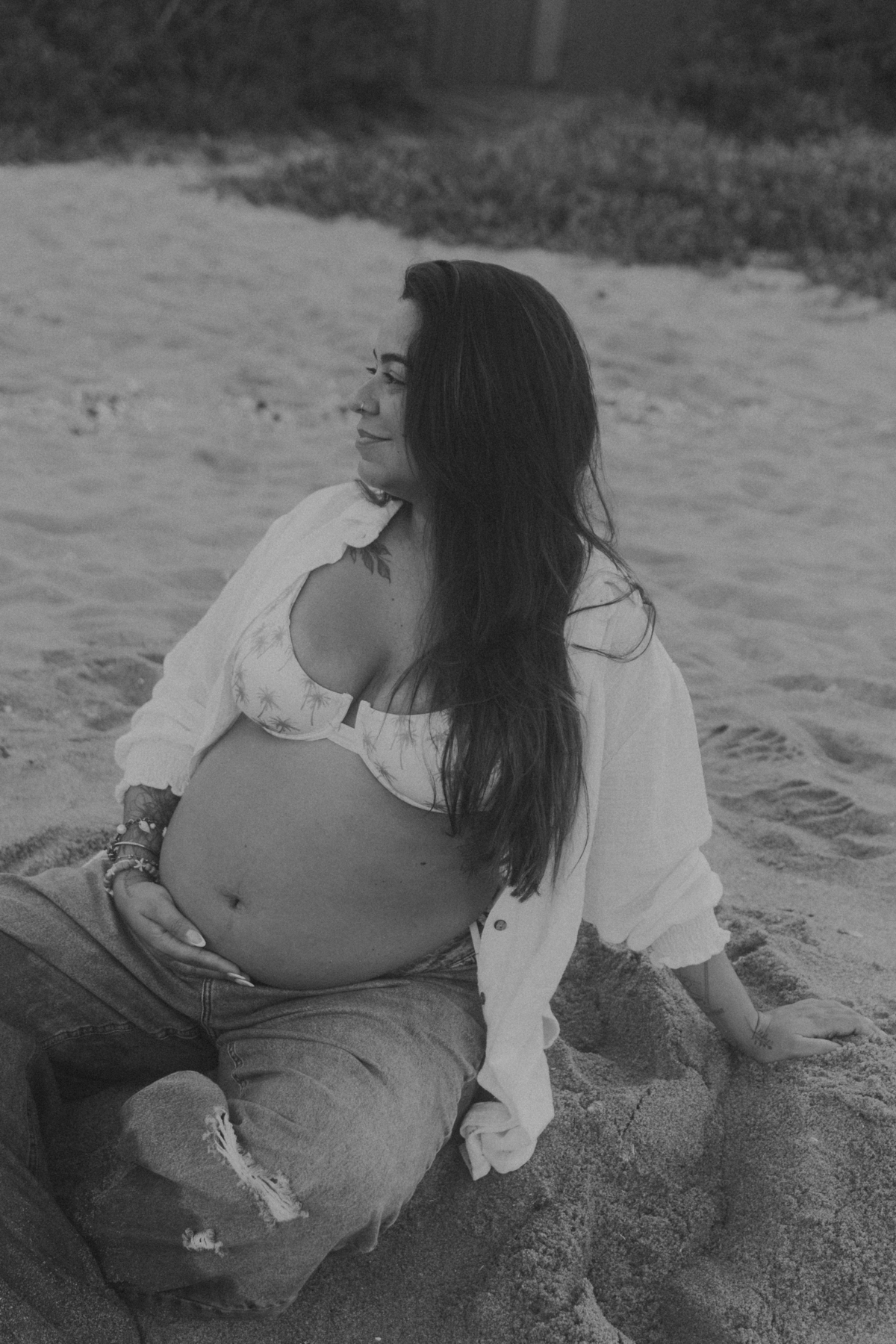 Gestante com mão na barriga durante ensaio na praia.
