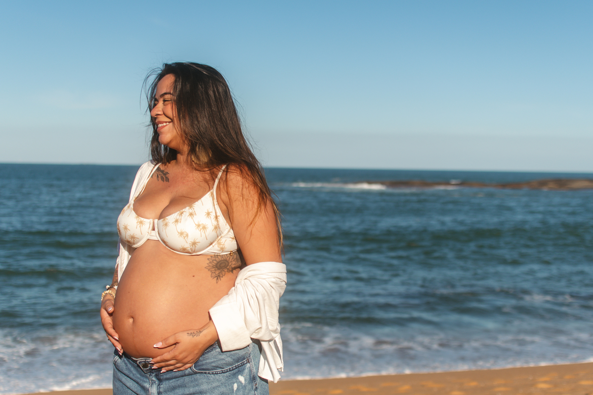 Gestante sorrindo em ensaio fotográfico na praia.
