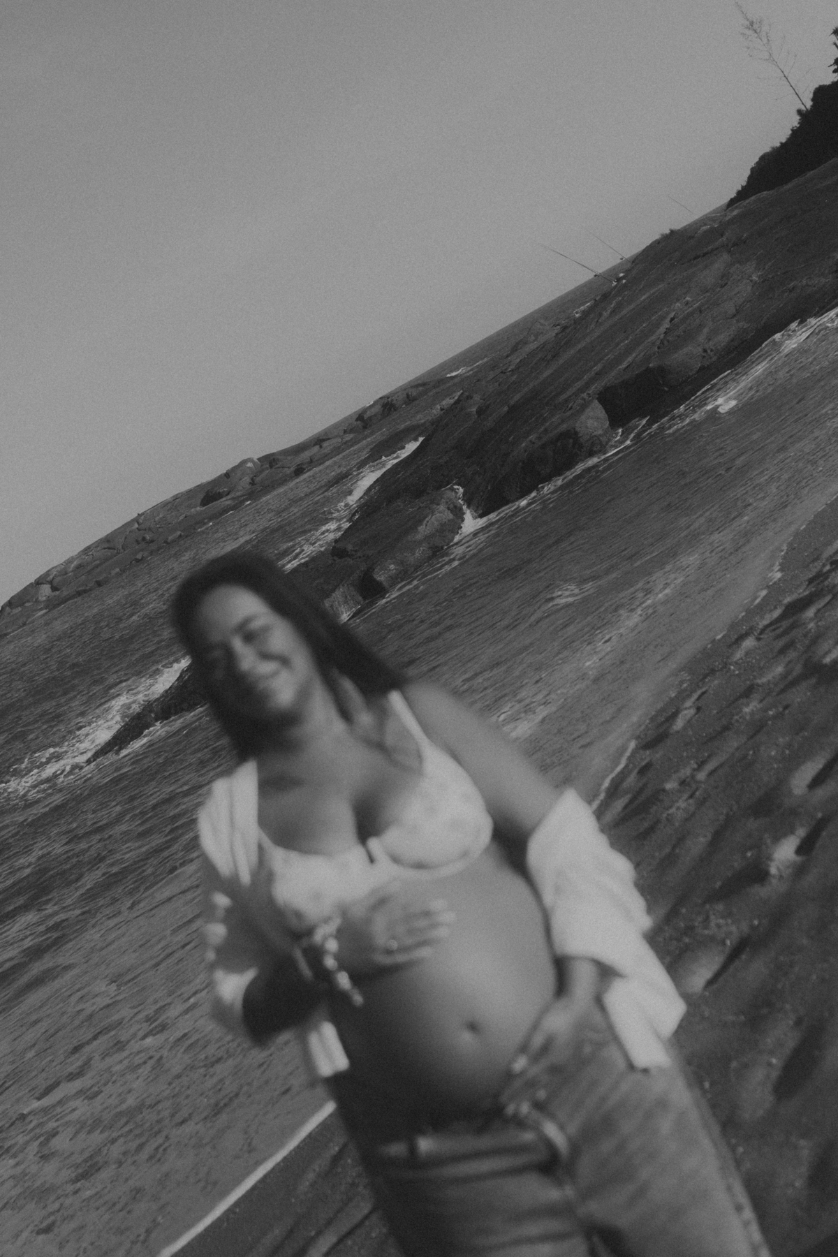 Foto preto e branco conceitual de gestante na praia com mar ao fundo.