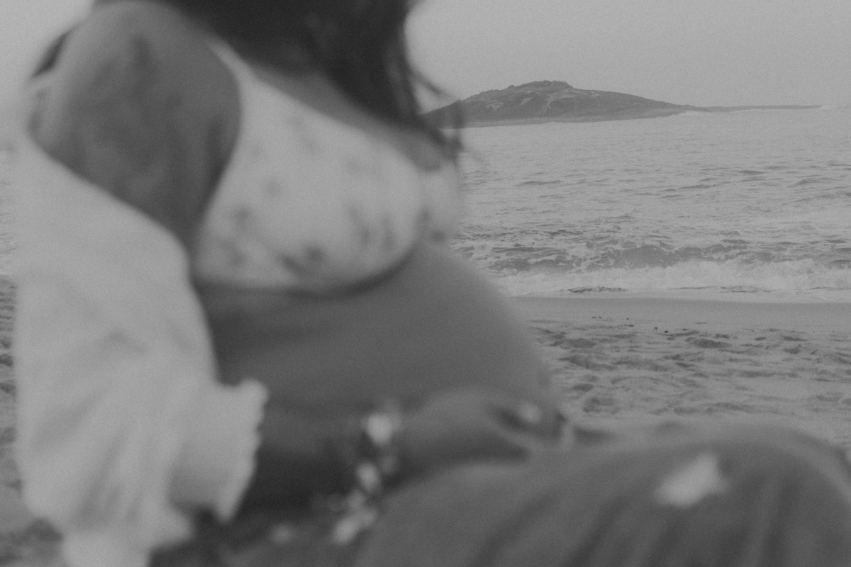 Gestante sentada na areia em ensaio fotográfico preto e brando.