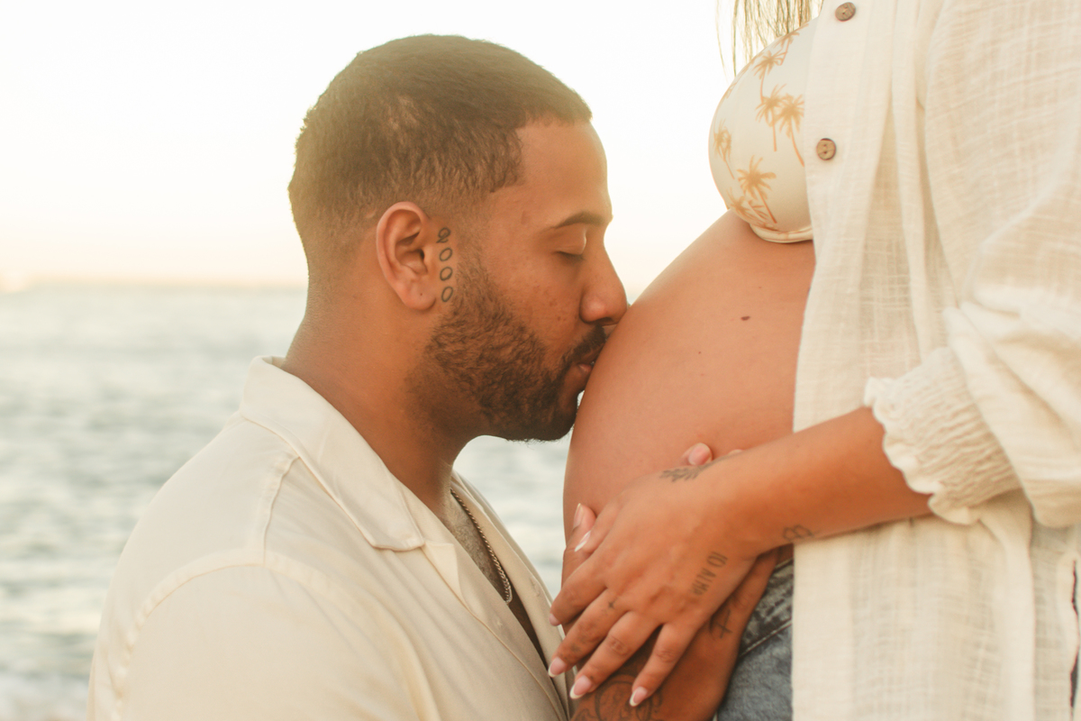 Close do marido beijando a barriga da esposa grávida durante ensaio de gestante.