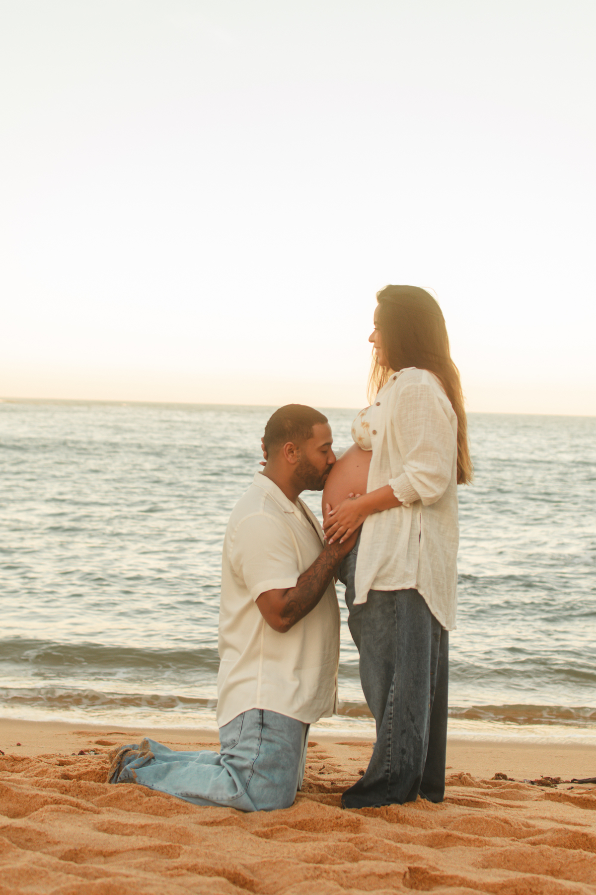 Pai beijando a barrida da gestante durante o ensaio no pôr do sol.