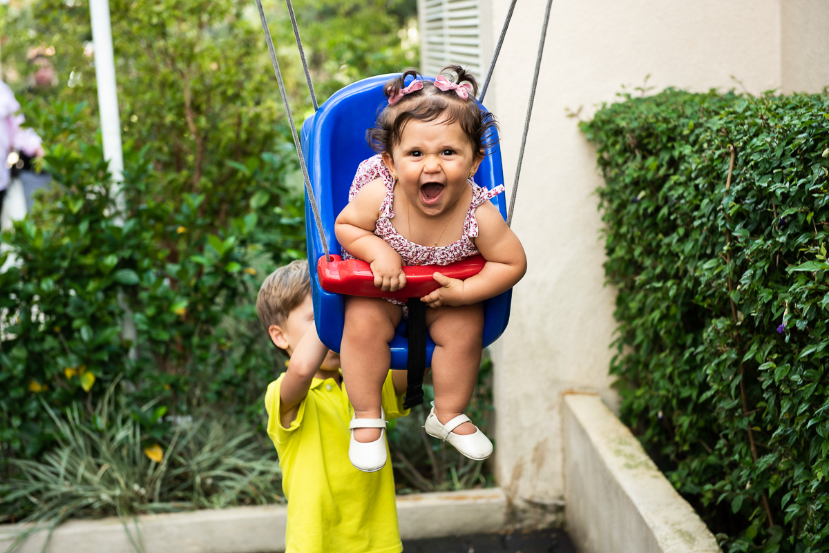 menino de blusa amarela empurrando a bebê no balanço
